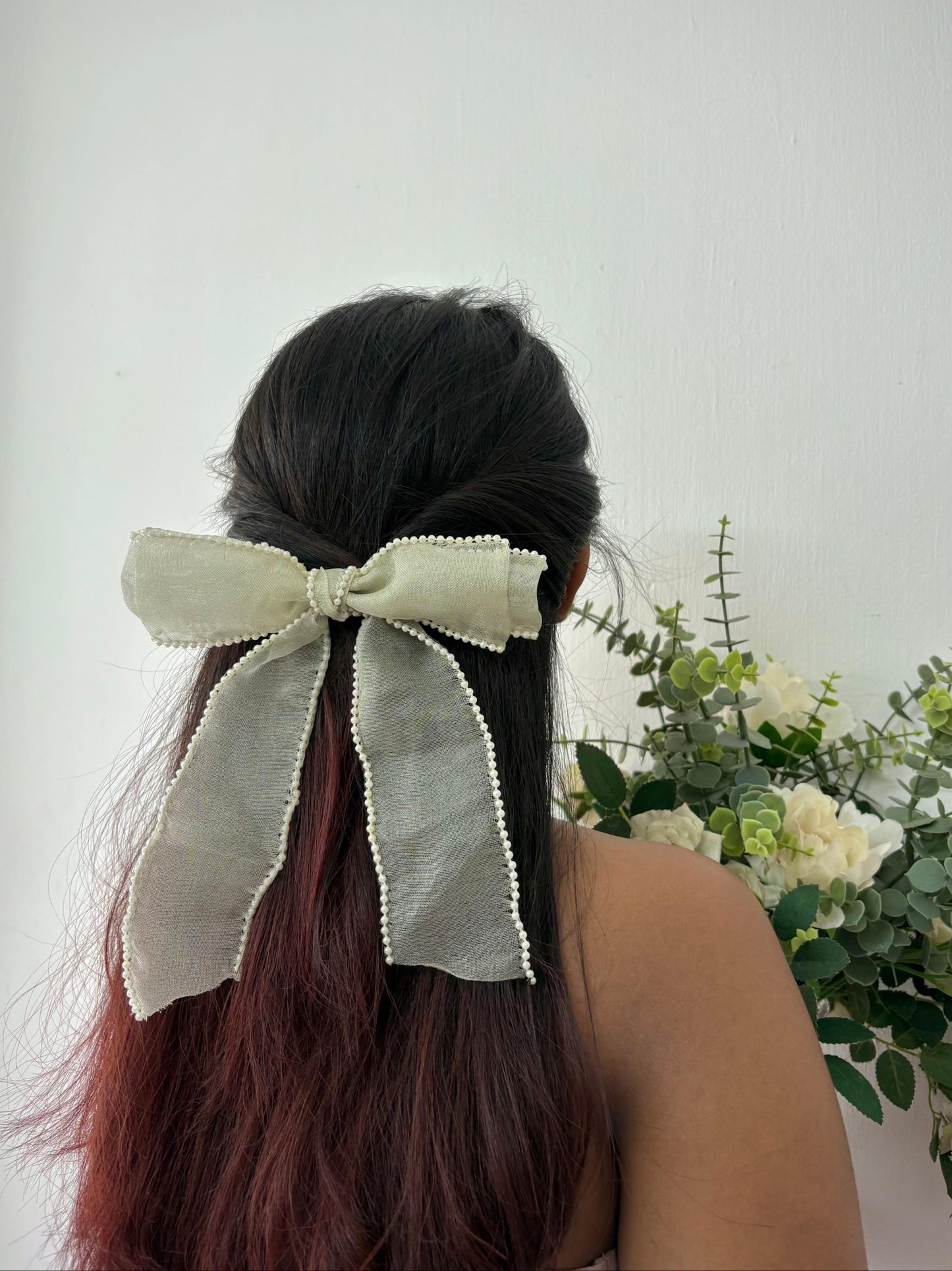 Person with a large bow in their hair against a light background with flowers.