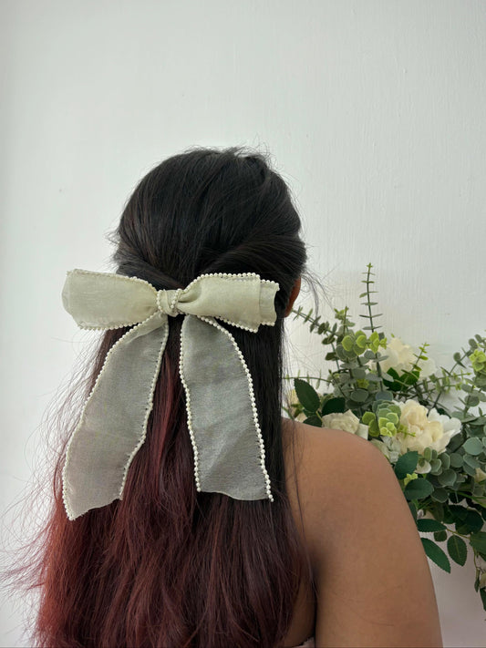 Person with a large bow in their hair against a light background with flowers.